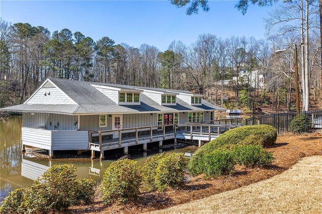 back of property with a shingled roof, a deck with water view, and fence