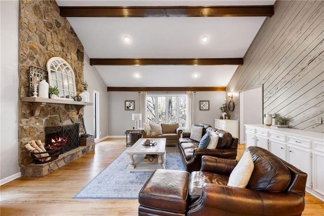 living room with beam ceiling, a stone fireplace, and light wood-style floors