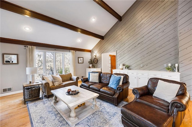 living area with visible vents, beamed ceiling, high vaulted ceiling, light wood-style floors, and baseboards