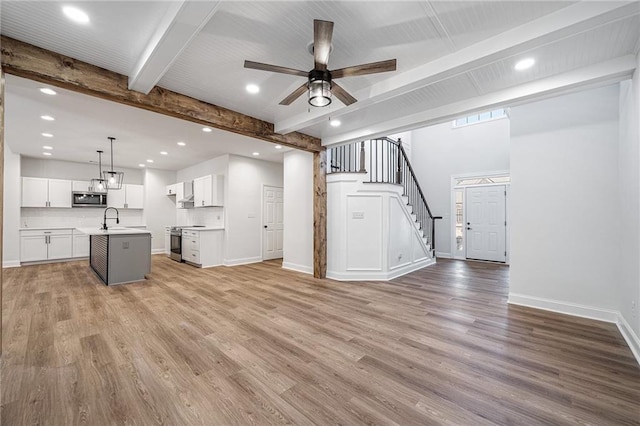 unfurnished living room with beam ceiling, light wood-style floors, a sink, baseboards, and stairs