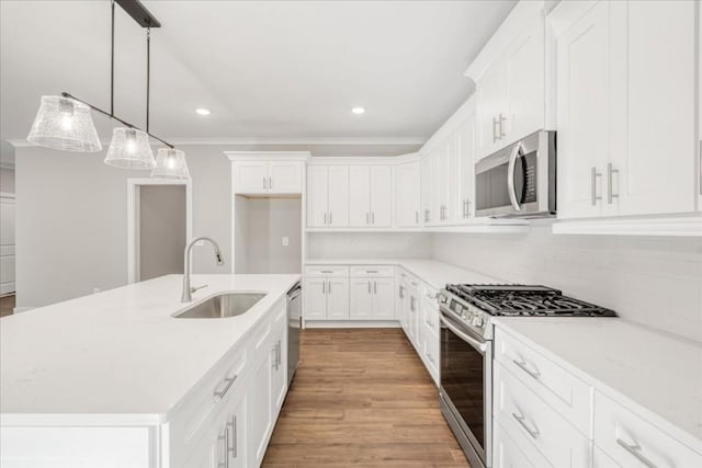 kitchen with stainless steel appliances, a kitchen island with sink, sink, pendant lighting, and white cabinetry