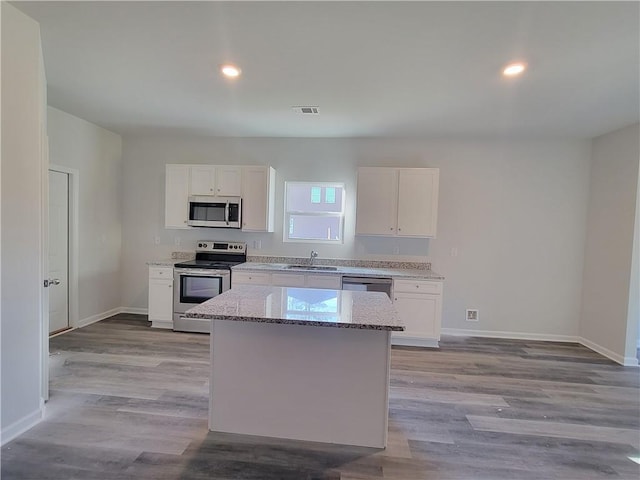 kitchen with appliances with stainless steel finishes, white cabinets, a kitchen island, and sink