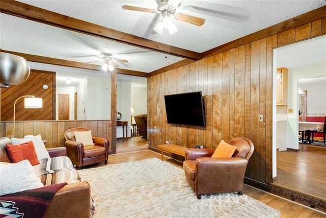 living room with beamed ceiling, light hardwood / wood-style floors, a textured ceiling, and wood walls