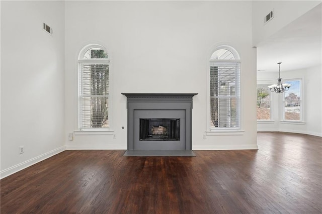 unfurnished living room with dark wood-style floors, a fireplace with flush hearth, visible vents, and a chandelier