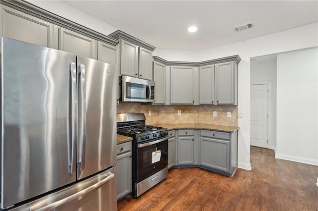 kitchen with dark wood finished floors, gray cabinets, backsplash, appliances with stainless steel finishes, and dark stone countertops