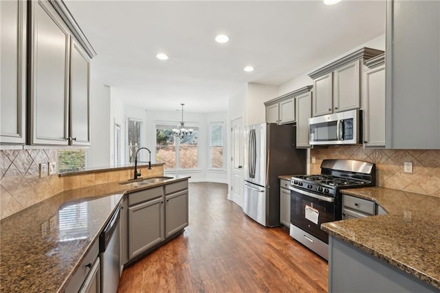 kitchen with gray cabinetry, stainless steel appliances, a sink, and pendant lighting