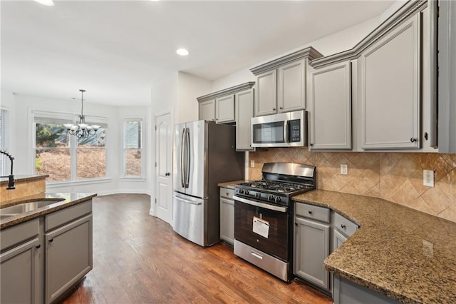 kitchen featuring appliances with stainless steel finishes, dark stone countertops, a sink, and gray cabinetry