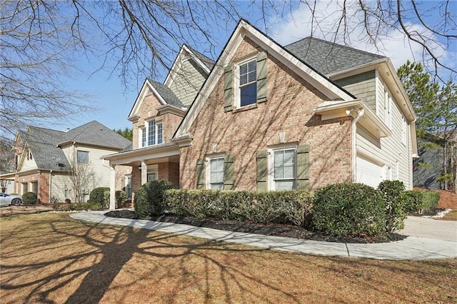 view of side of property featuring a garage, brick siding, a lawn, and a shingled roof