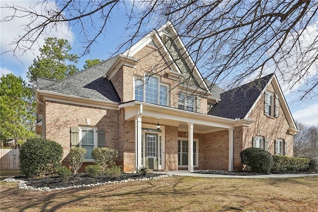 view of front of property with a shingled roof, a front yard, covered porch, and brick siding