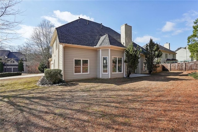 rear view of house with a yard, a chimney, fence, and roof with shingles