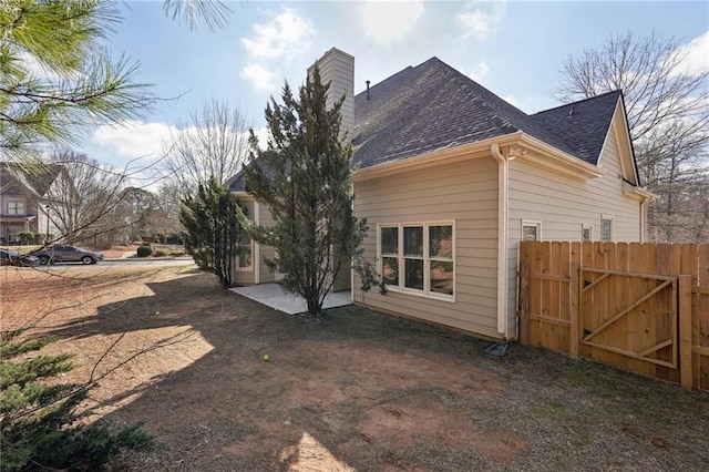 view of side of property featuring a patio area, a shingled roof, a gate, and fence