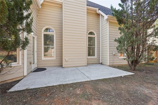 back of property with roof with shingles and a patio area