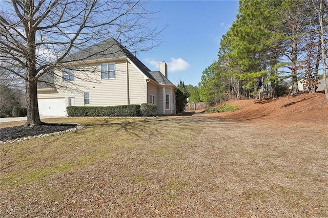 view of side of home featuring a garage, a lawn, and a chimney