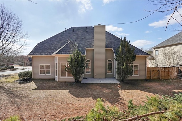 rear view of house with roof with shingles, a chimney, a patio area, and fence