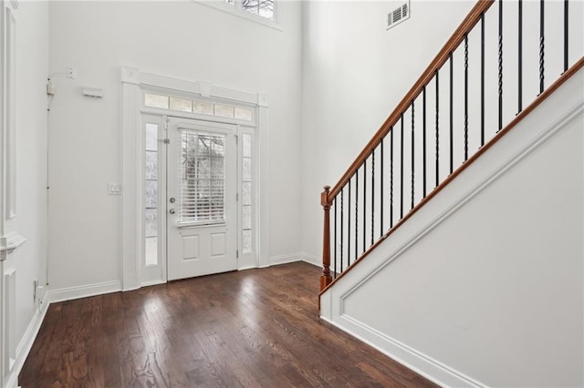 foyer entrance with dark wood-style flooring, a towering ceiling, visible vents, stairs, and baseboards