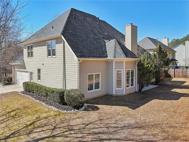 back of property with an attached garage, roof with shingles, and a chimney