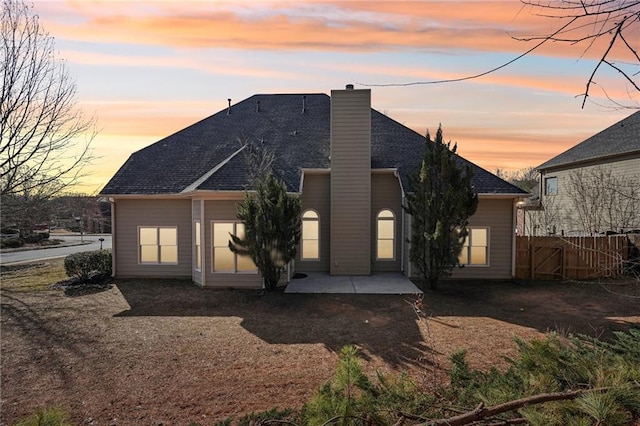 rear view of property featuring a shingled roof, a patio area, fence, and a chimney