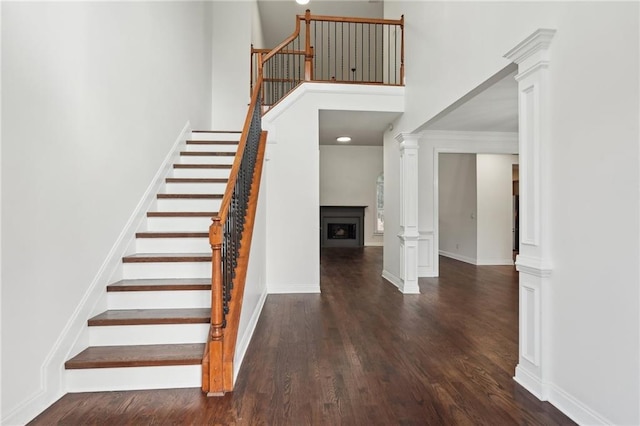 stairs with a fireplace, decorative columns, a towering ceiling, and wood finished floors