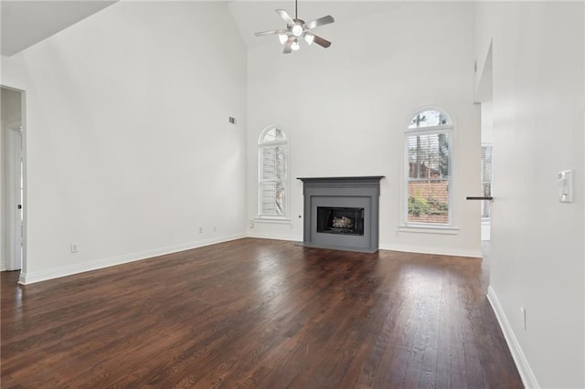 unfurnished living room featuring high vaulted ceiling, dark wood-type flooring, a fireplace with flush hearth, a ceiling fan, and baseboards