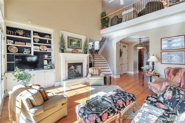 living area featuring light wood-type flooring, a towering ceiling, arched walkways, and a glass covered fireplace