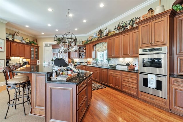 kitchen with double oven, brown cabinetry, a sink, and a kitchen bar