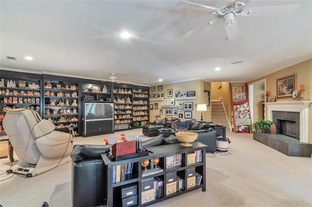 carpeted living area with stairs, a tiled fireplace, visible vents, and a ceiling fan