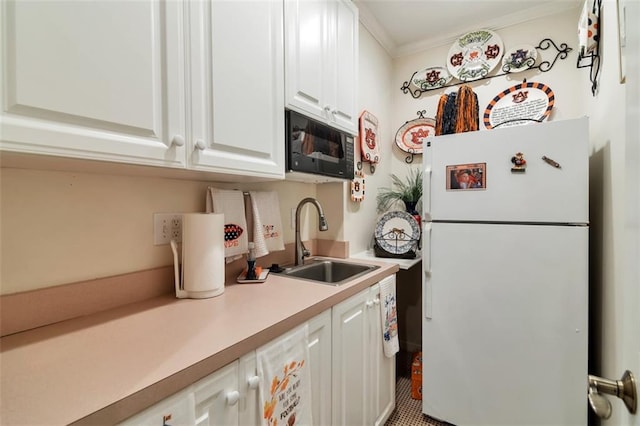 kitchen featuring light countertops, freestanding refrigerator, white cabinets, a sink, and black microwave