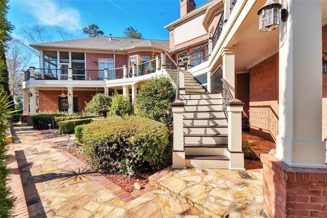 back of property featuring stairs, a chimney, and brick siding