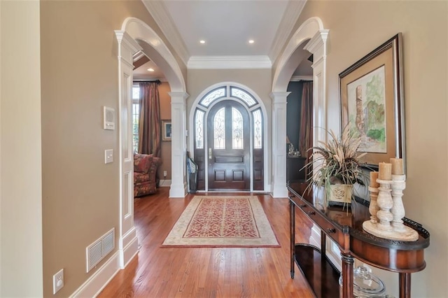 entrance foyer with arched walkways, visible vents, decorative columns, and wood finished floors