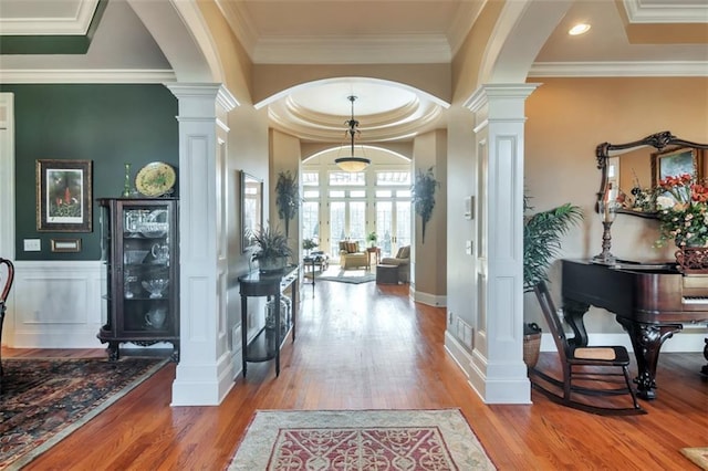 foyer entrance featuring decorative columns, ornamental molding, and wood finished floors