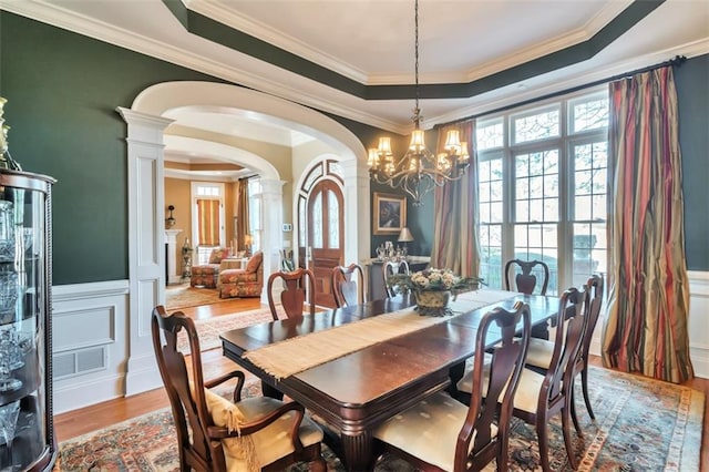 dining area with arched walkways, a wainscoted wall, decorative columns, and a tray ceiling