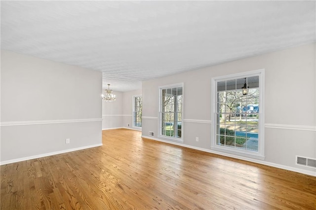 spare room with visible vents, baseboards, wood finished floors, and a chandelier