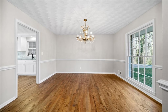 unfurnished dining area with visible vents, baseboards, an inviting chandelier, wood finished floors, and a sink