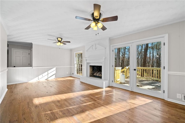 unfurnished living room featuring ceiling fan, a fireplace, wood finished floors, and crown molding