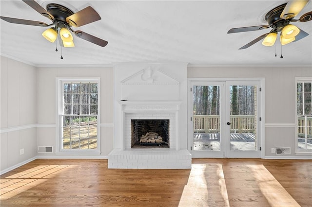 unfurnished living room with a fireplace, crown molding, wood finished floors, and visible vents