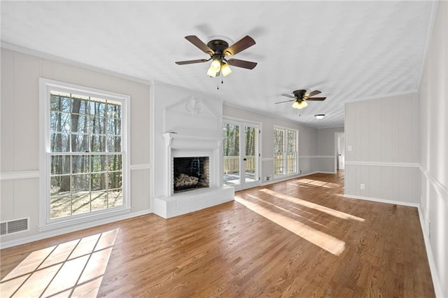 unfurnished living room featuring visible vents, a brick fireplace, ceiling fan, wood finished floors, and a decorative wall