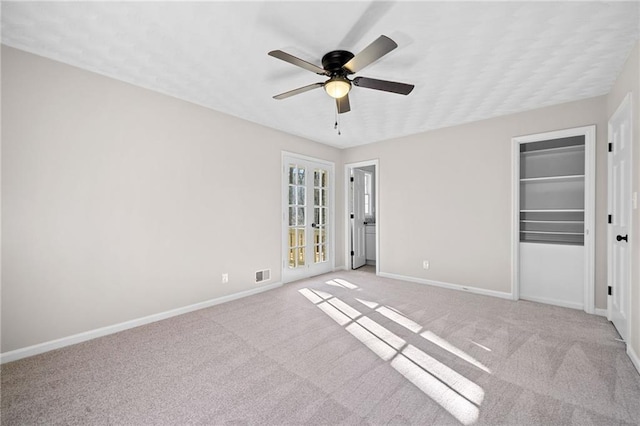 empty room featuring visible vents, light colored carpet, a ceiling fan, and baseboards