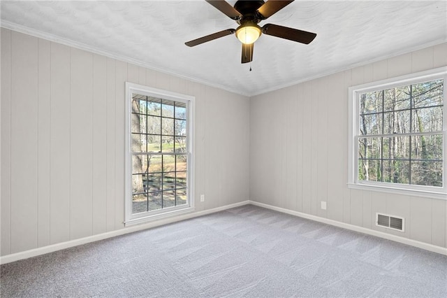 carpeted empty room with visible vents, baseboards, ceiling fan, and crown molding