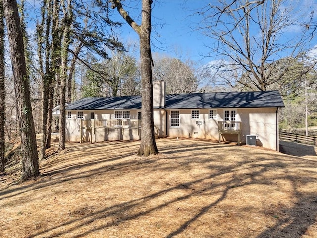 back of property featuring fence, central AC unit, brick siding, and a chimney