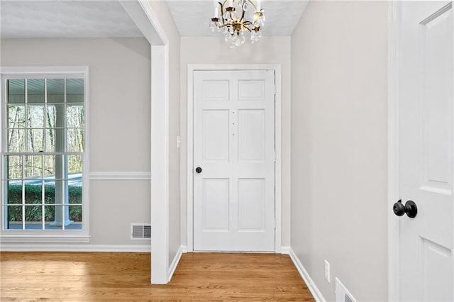 foyer entrance featuring visible vents, baseboards, light wood-style flooring, and a chandelier