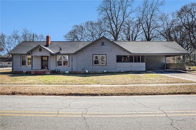 ranch-style home featuring roof with shingles, a chimney, concrete driveway, a carport, and a front lawn