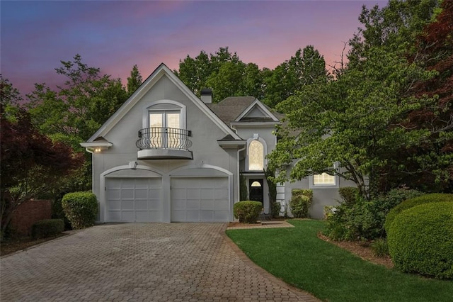 view of front facade with a balcony, stucco siding, decorative driveway, an attached garage, and a chimney