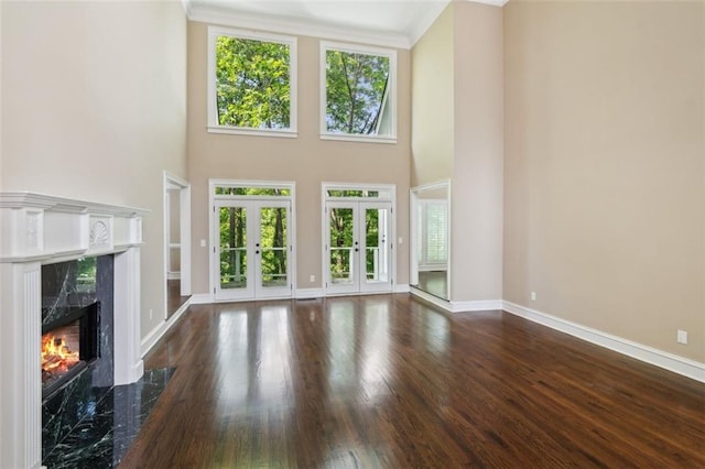 unfurnished living room featuring plenty of natural light, french doors, baseboards, a fireplace, and a towering ceiling
