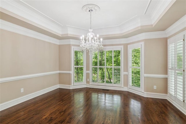 empty room featuring a chandelier, a tray ceiling, wood finished floors, ornamental molding, and baseboards