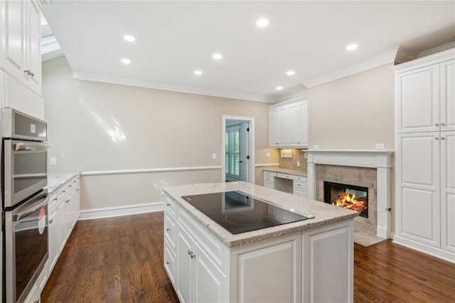 kitchen featuring black electric cooktop, double oven, ornamental molding, white cabinetry, and a kitchen island