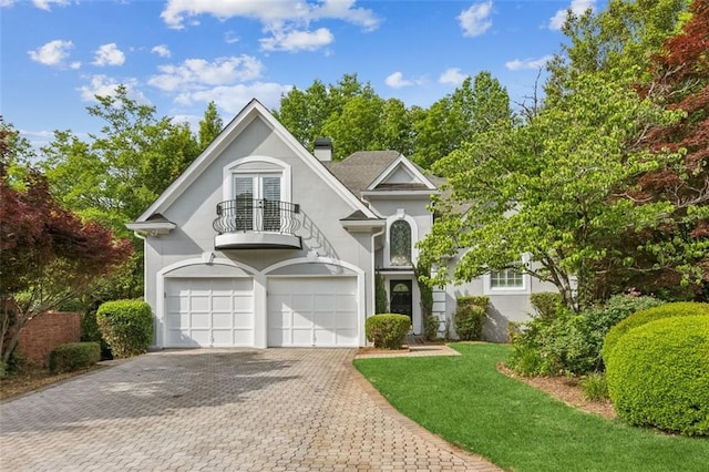 view of front of property with a balcony, stucco siding, decorative driveway, french doors, and a chimney