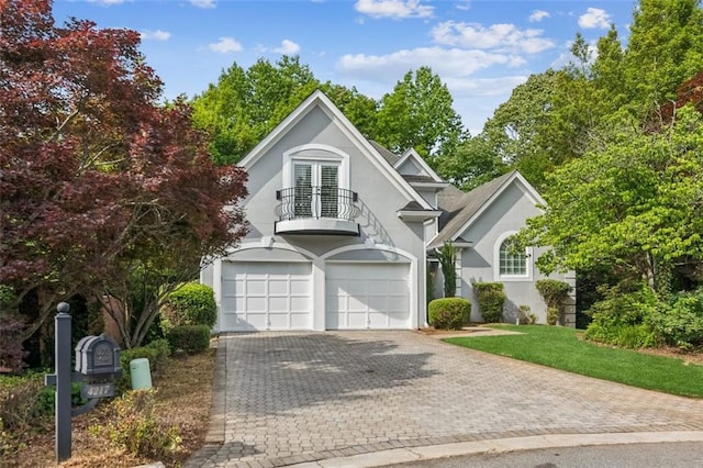 view of front facade with a balcony, french doors, a garage, stucco siding, and decorative driveway