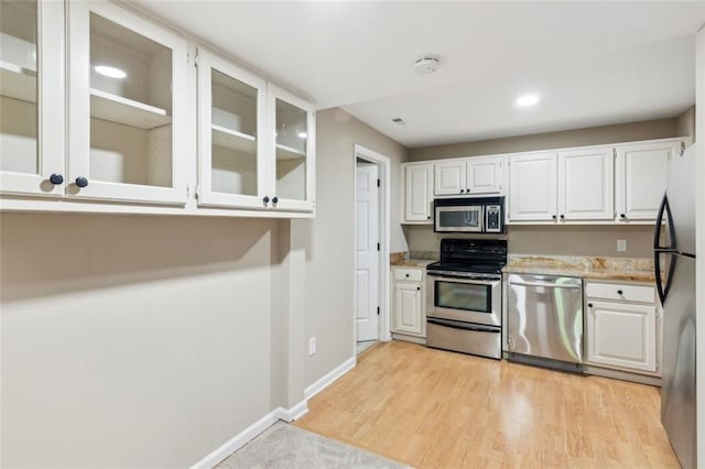 kitchen featuring stainless steel appliances, white cabinetry, glass insert cabinets, light wood-type flooring, and baseboards