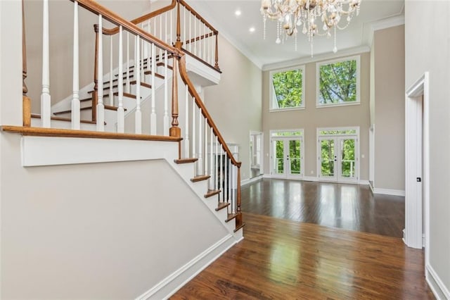 stairs with wood finished floors, baseboards, a towering ceiling, ornamental molding, and a chandelier