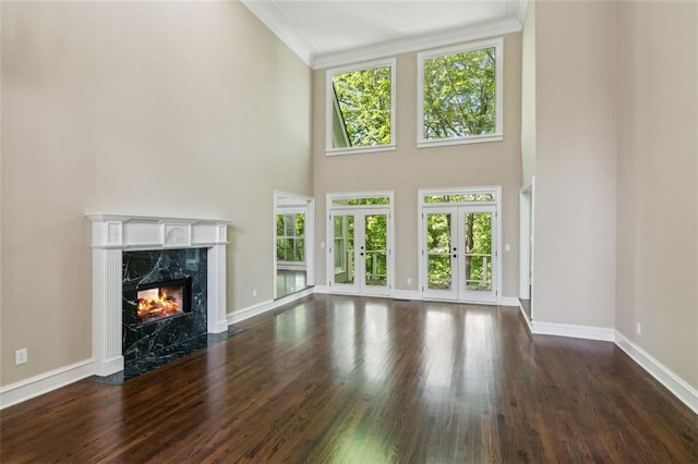 unfurnished living room featuring a high end fireplace, crown molding, baseboards, wood finished floors, and french doors